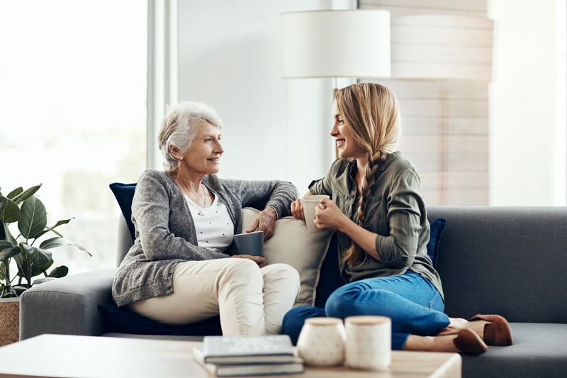 Two women talk on a couch with coffee.