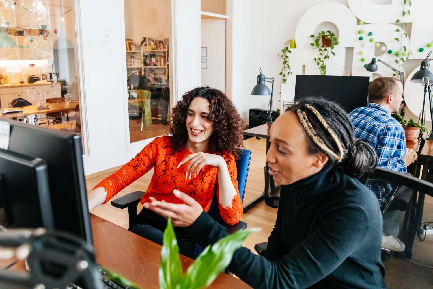 A transgender woman smiling while working at a computer desk with one of her colleagues