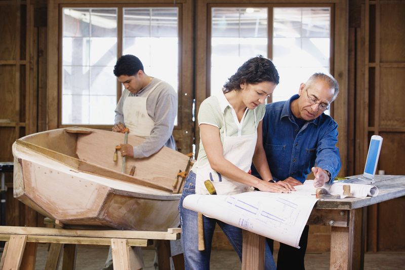 Two young people and an older man reviewing plans to make a boat in a workshop