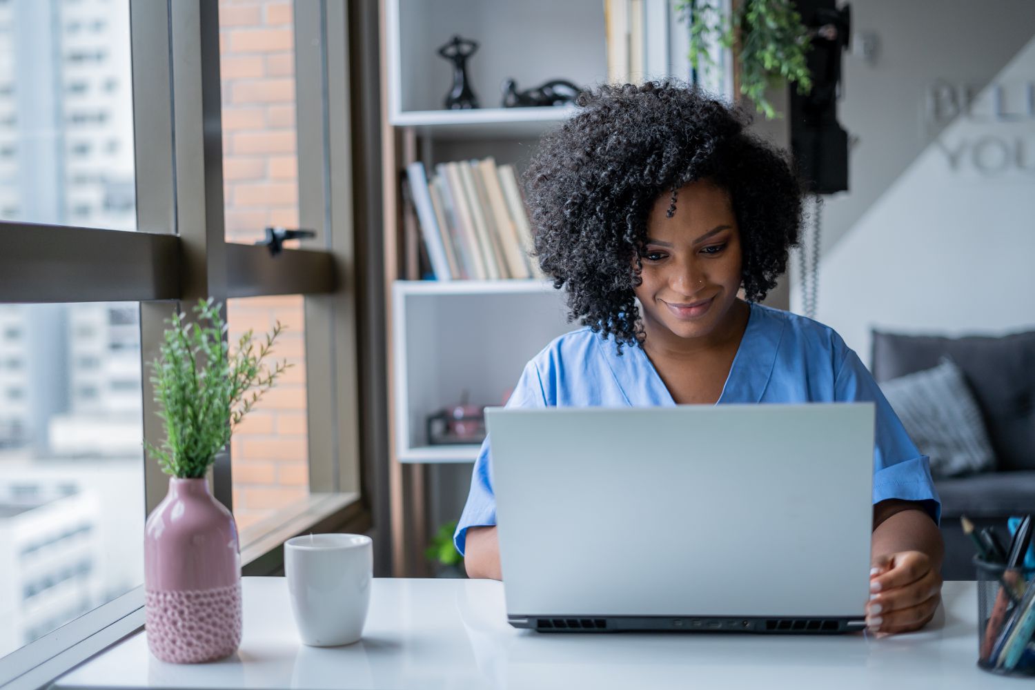 Young woman in her living room, looking at her laptop with a smile