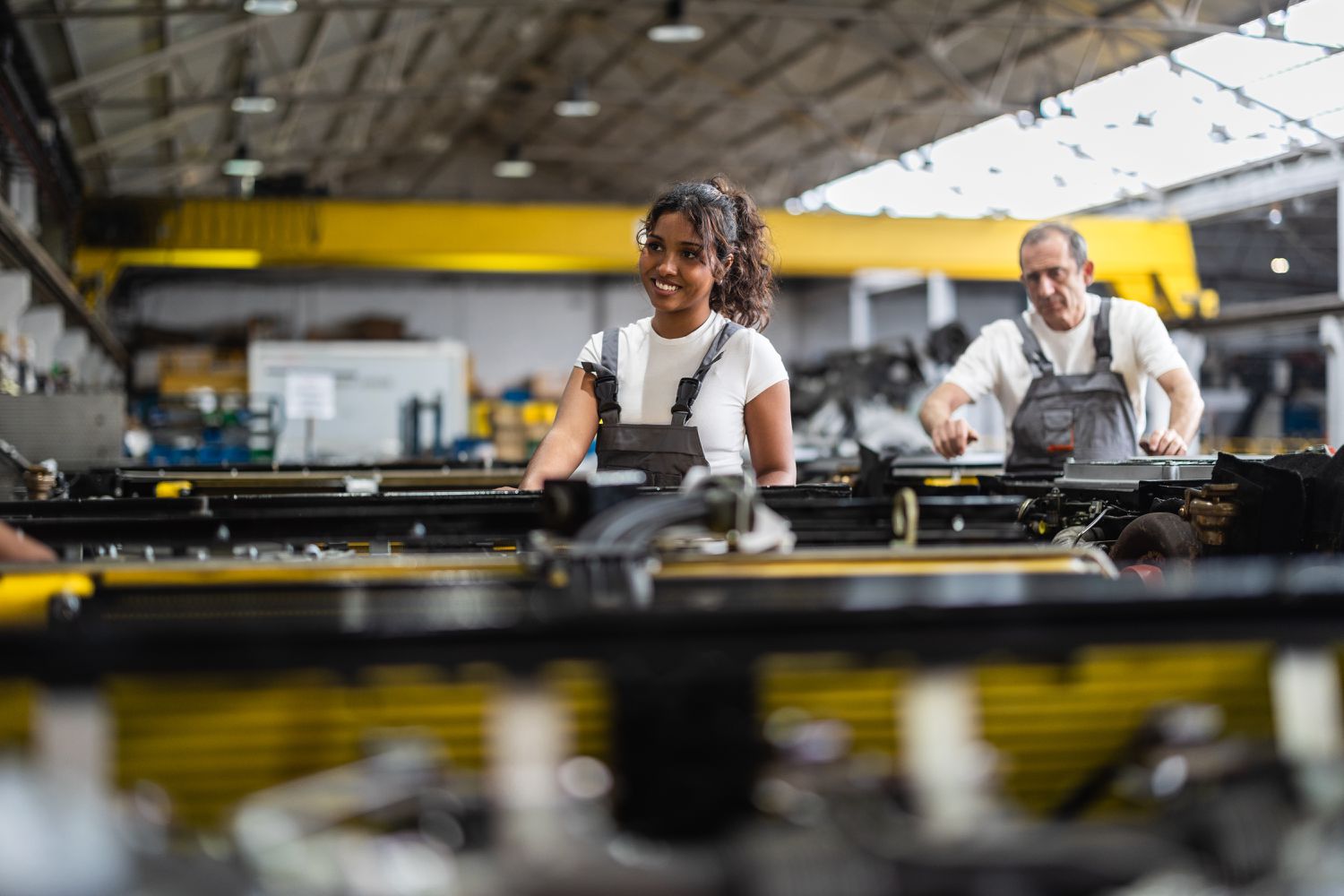 Smiling factory workers collaborate on assembling car parts along a modern production line in an advanced automotive manufacturing facility
