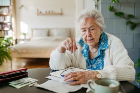 A worried looking widow sits at a tabel in their home reviewing their finances.
