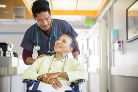 A male nurse pushes a senior woman in a wheelchair.