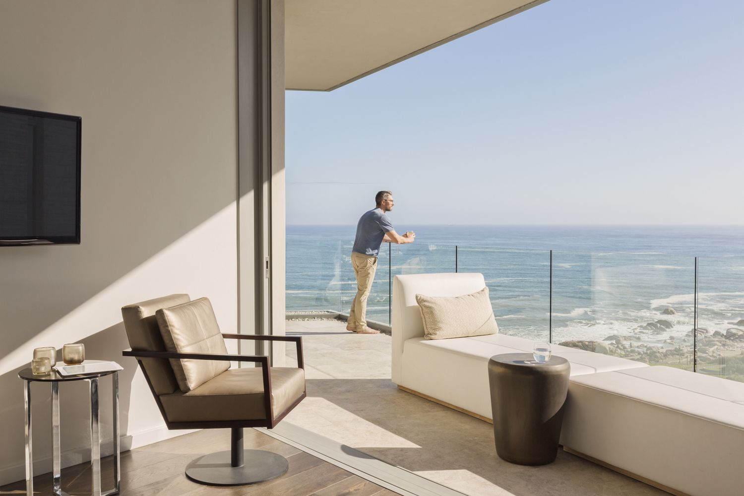 Man enjoying sunny ocean view from luxury balcony.