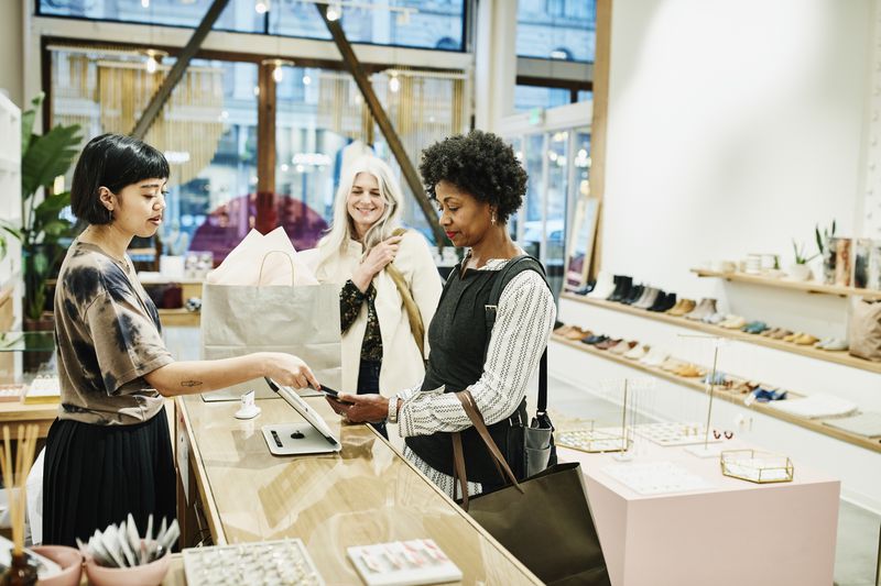 Woman paying with smartphone after shopping in boutique with friend