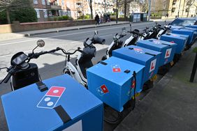 The Domino's Pizza logo is seen on boxes on the back of several delivery bikes on a street.
