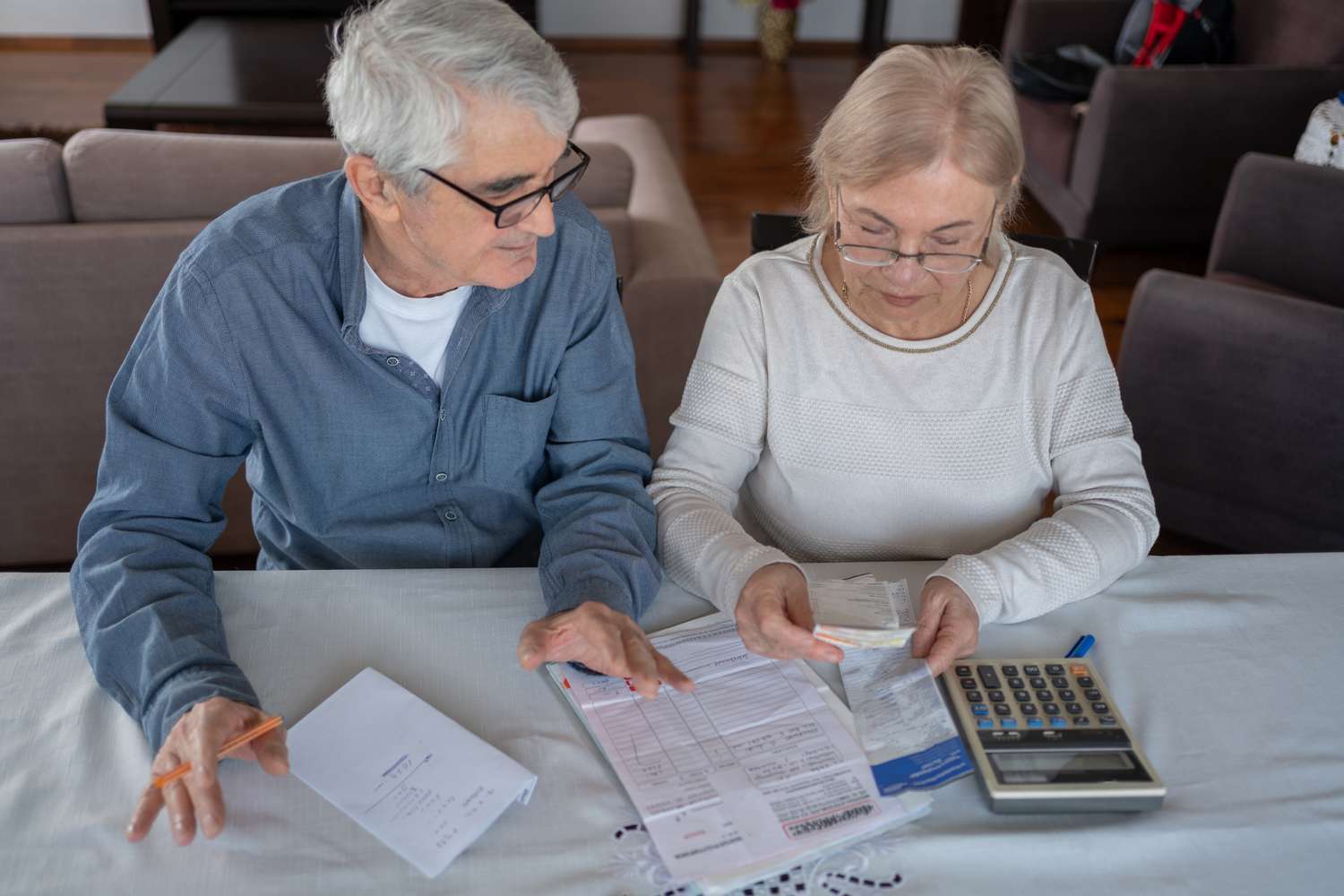 A senior couple sits at a table with a calculator and some documents.