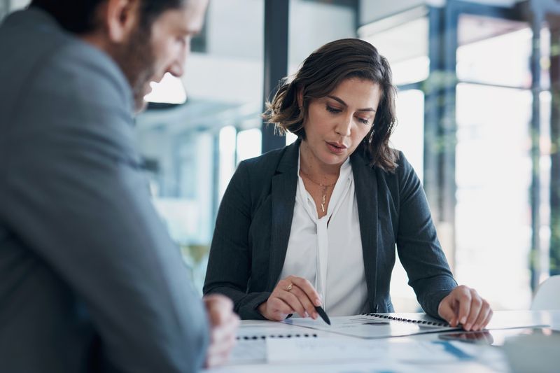 Business professionals review paperwork while sitting in a glass conference room.