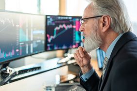 A mature male stock broker staring intently at a computer monitor displaying charts and data.