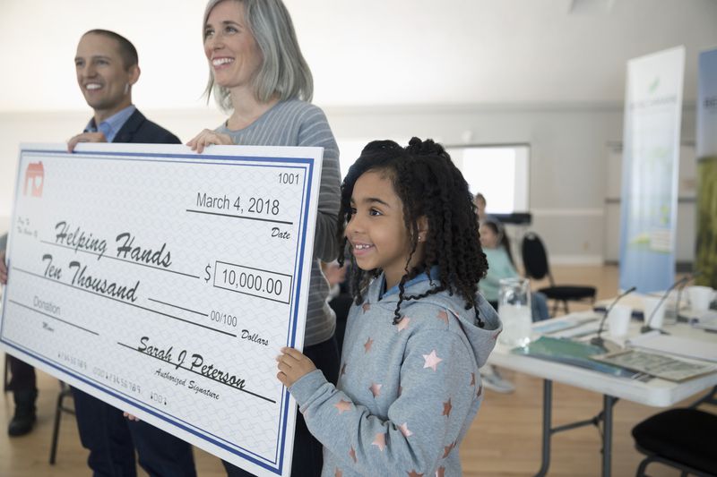 Girl helping hold large donation check in community center