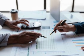 A couple of business people have pens pointing at documents on a table.