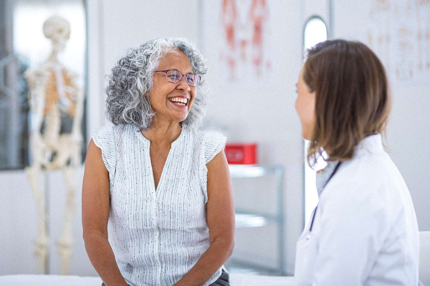 A vibrant and healthy senior woman of Hawaiian and Chinese descent smiles while talking with her female physician during a routine medical appointment.