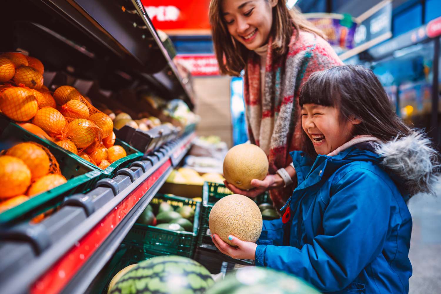 Mom & daughter choosing fresh organic fruit from the produce display racks while having groceries shopping in supermarket.
