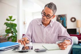 Mature man wearing eyeglasses at home using a credit card to make an online purchase