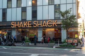 People walk on a sidewalk below the sign for a Shake Shack restaurant.