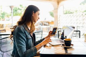 Image shows an investor using a laptop and a mobile phone to check up on investments while sitting at an outdoor cafe.