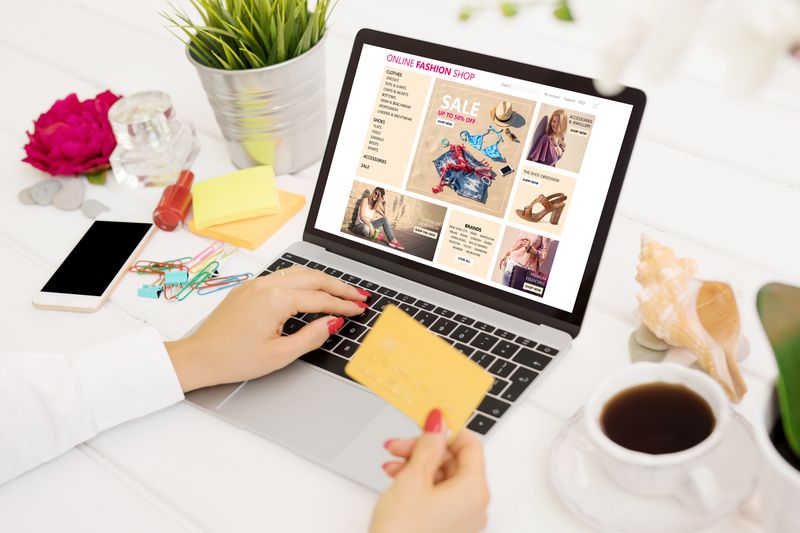 Woman with credit card buying new clothes online, view from above