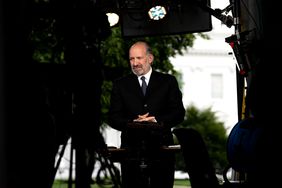 Howard Lutnick stands with his finders interlaced in front of his stomach. Cameras and lights surround him on the White House lawn.