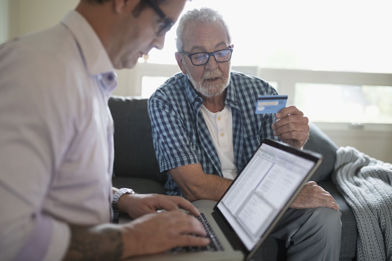 Two men looking at a credit card and a laptop