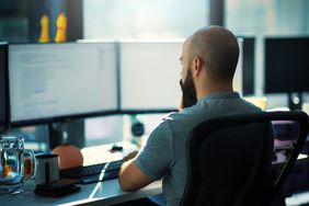 Close-up rear view of a young man coding on multiple computers