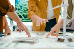 Close up of the hands of co-workers pointing to a large document lying on a table.