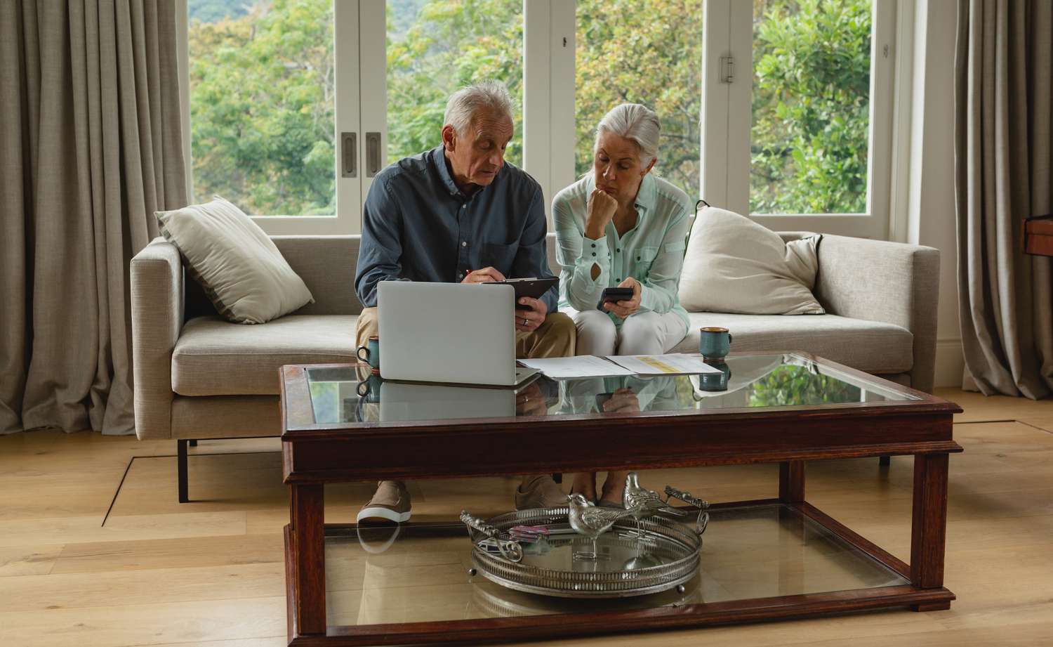  Senior couple looking at paperwork while sitting on a couch with a laptop on table in front of them