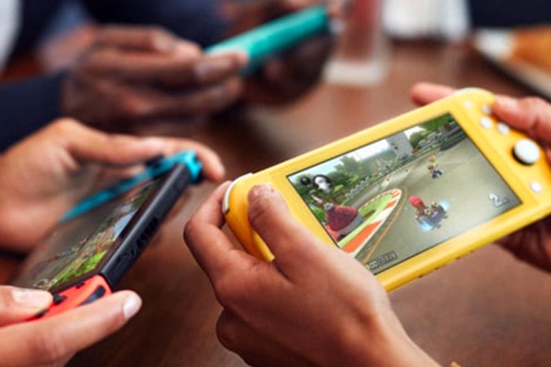Three people playing Super Mario Kart 8 on a Nintendo Switch and two Nintendo Switch Lite consoles.