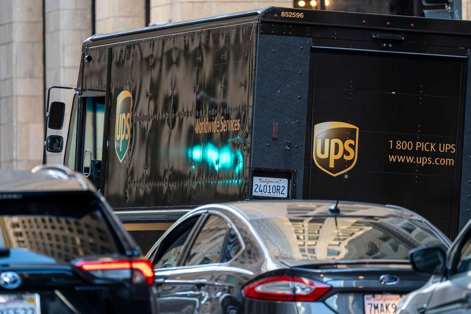 A brown UPS truck is seen on the road along with several cars.
