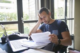 Many sitting at a desk holding his head and studying paperwork.