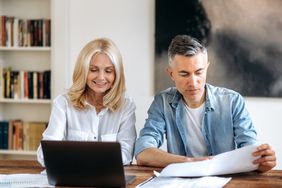 Couple in their 50s sitting at their dining table and looking at mortgage documents and a laptop