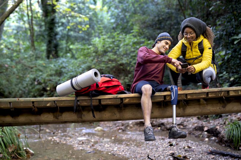 Man using a leg prosthesis with his girlfriend or friend spending a magnificent autumn day in the forest trekking or walking.