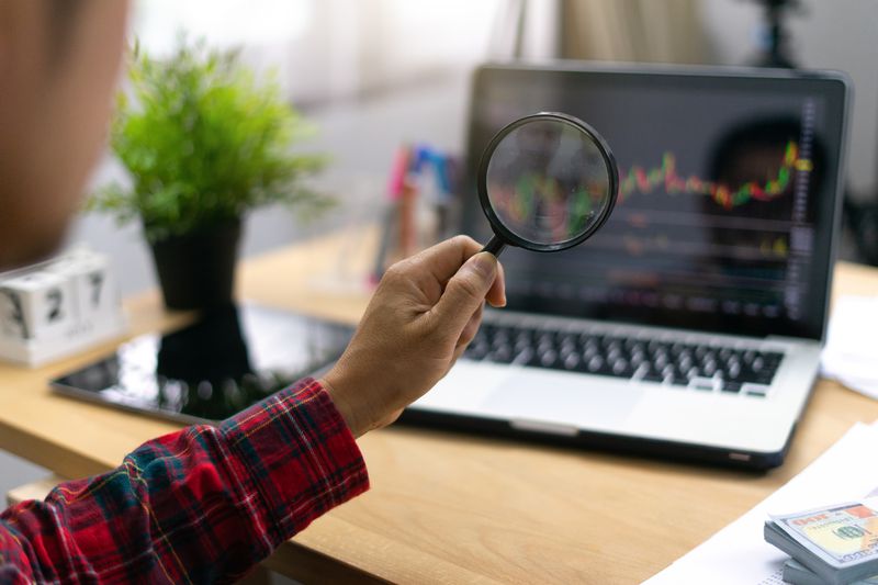 Investor looks at a stock chart on a laptop screen using a magnifying glass.