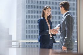 Two people in business suits in a downtown office building shaking hands. 
