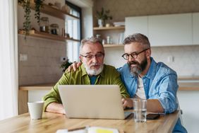 Mature son helping father to manage his finance, teaching how to work with internet baking and shopping online.
