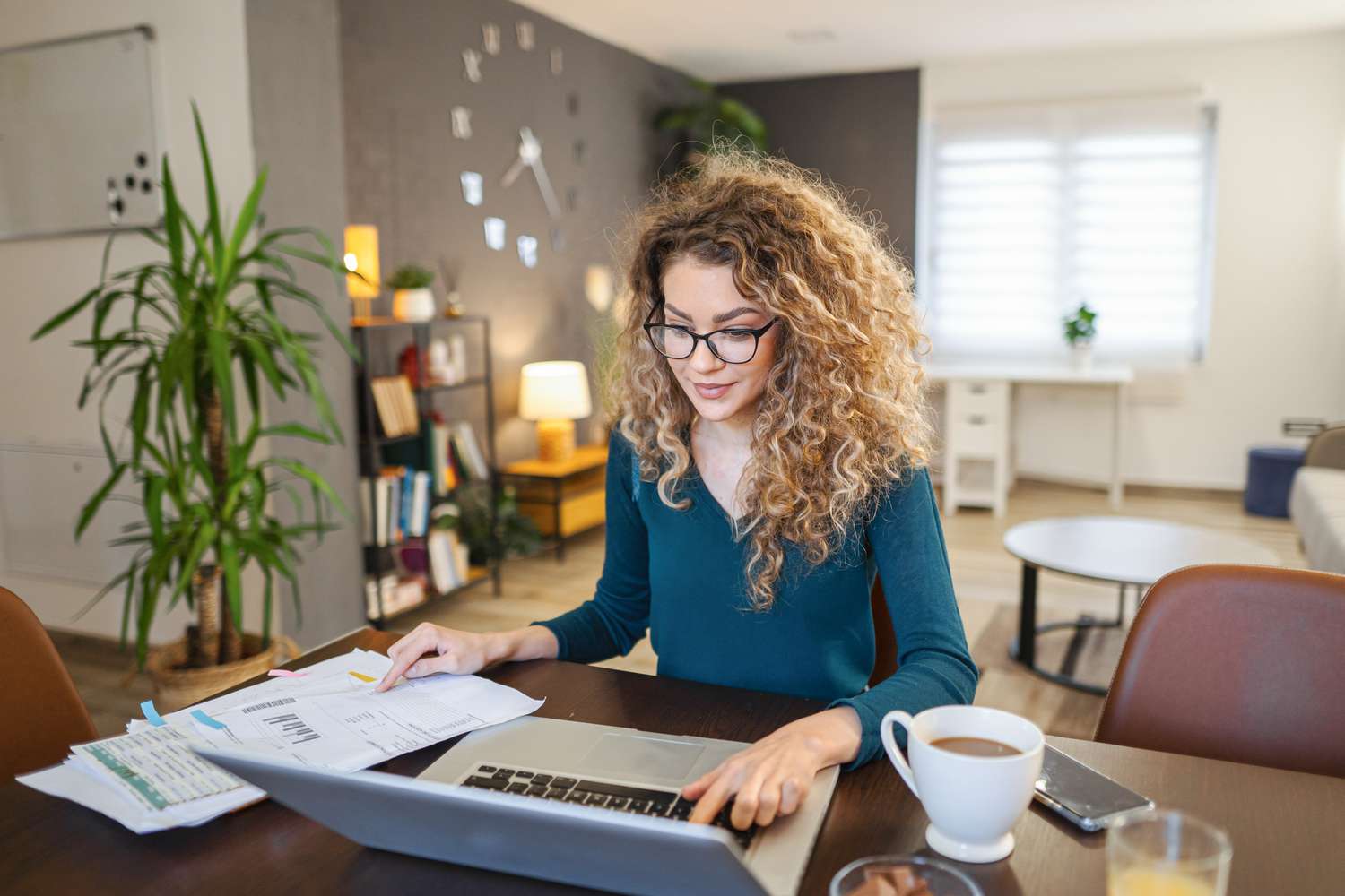 Woman with spectacles looking at paperwork and laptop 
