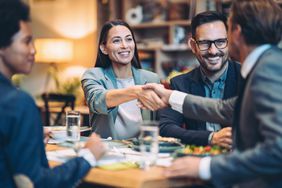 Business people sitting around a table shake on a deal