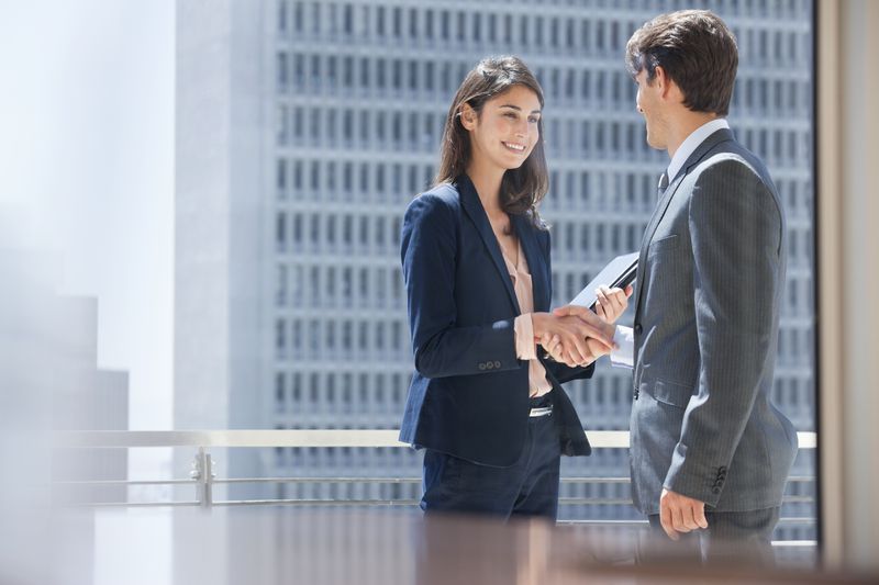 Two people in business suits in a downtown office building shaking hands. 