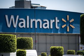 The blue and white Walmart logo is seen on the side of a store, with green bushes in the foreground.