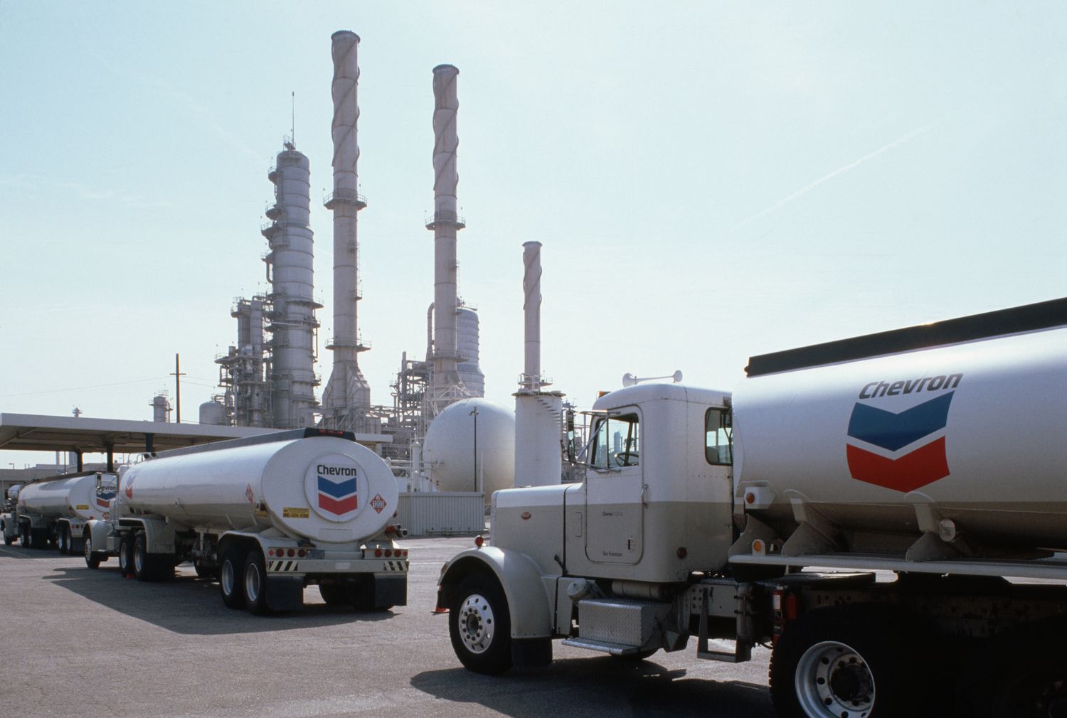 Three Chevron oil trucks line up outside the refinery in California