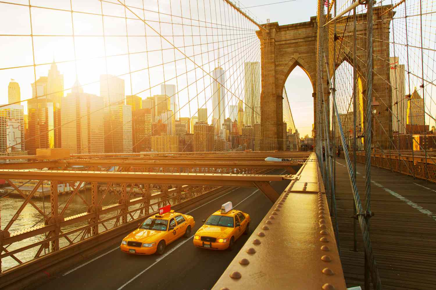 Taxis on the Brooklyn Bridge at sunset in New York City, with the Freedom Tower and Manhattan Financial District in the background
