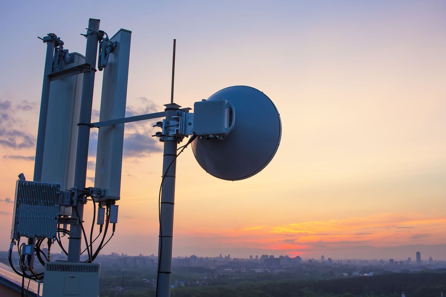 A base station with a radio relay antenna on the background of a sunset over the city