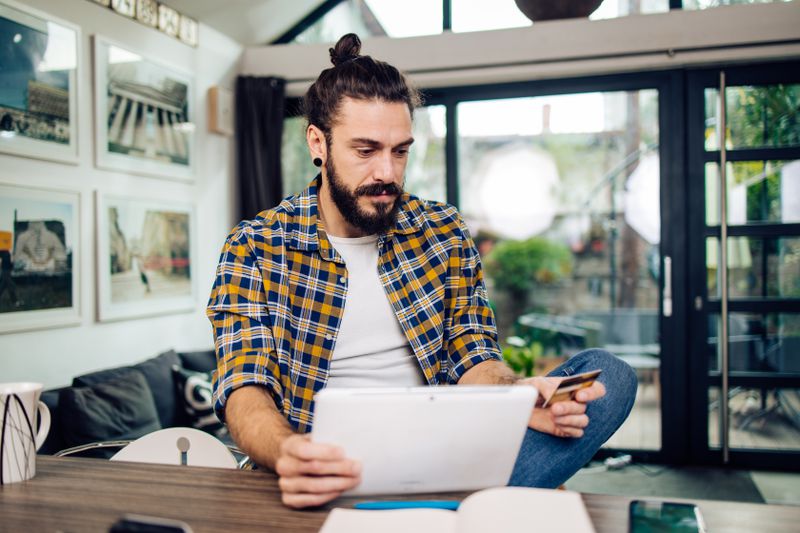 Hippie man looking at his credit card statement sitting at home