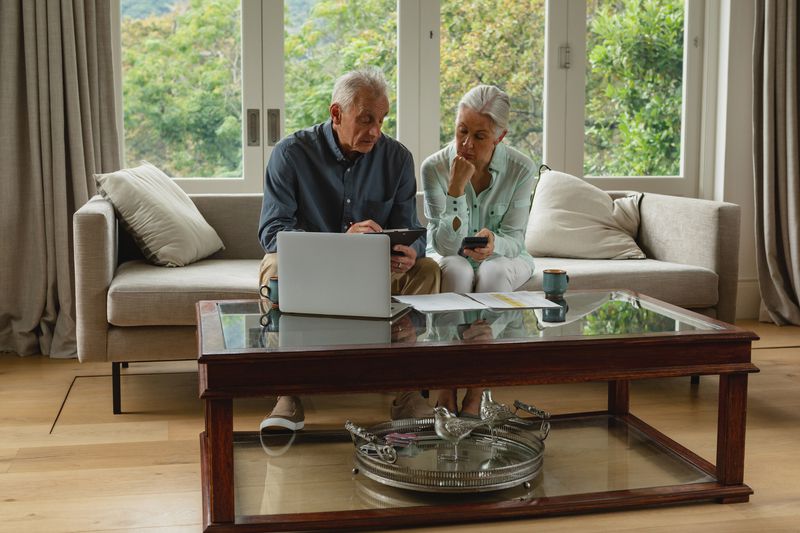 Senior couple looking at paperwork while sitting on a couch with a laptop on table in front of them
