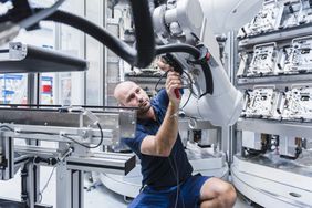 Engineer working in a factory with a robotic arm.