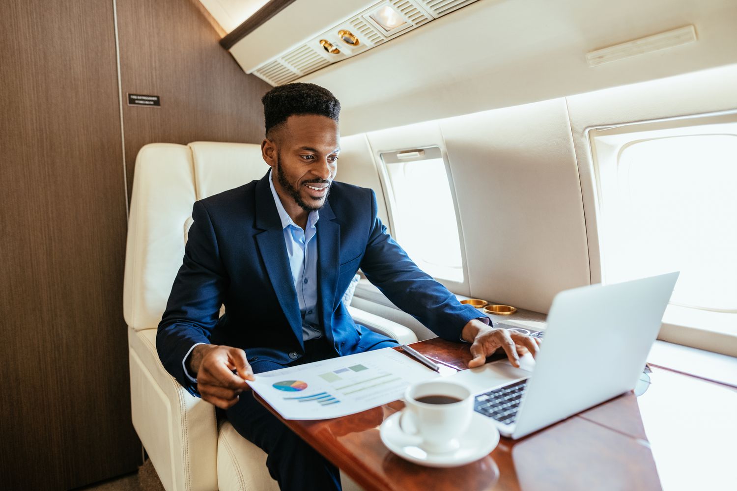 A private venture capitalist uses a laptop and reviews a business prospectus while flying on a private jet.