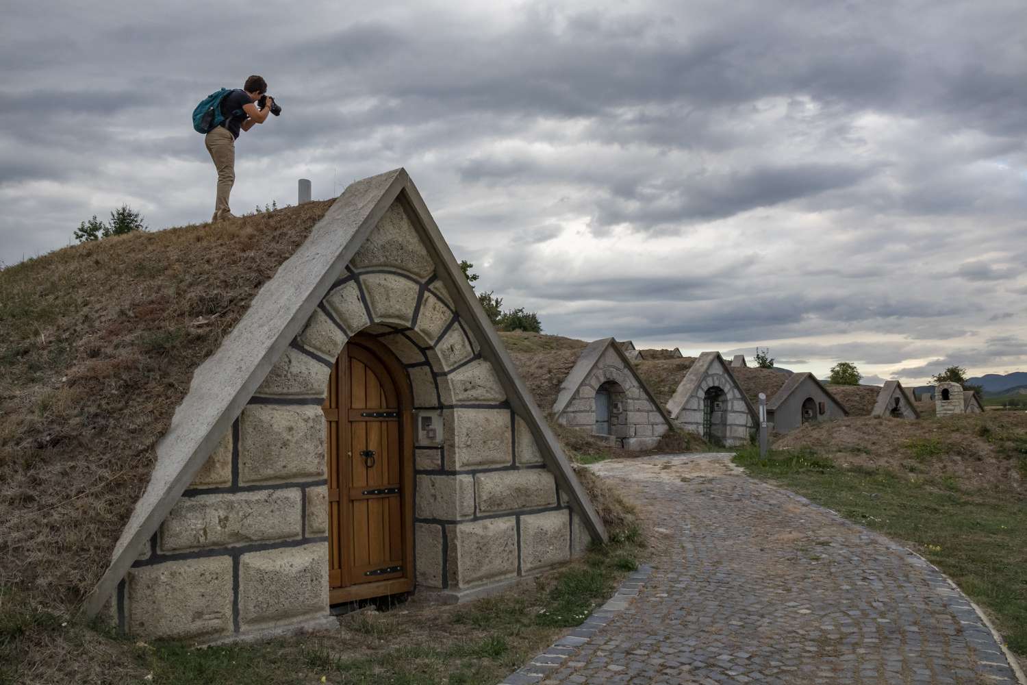 Person photographing small, triangular-roofed buildings extending along a cobblestone pathway