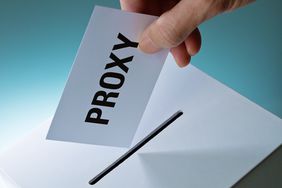 A hand dropping a proxy vote into a proxy ballot box. Photographed on white background.