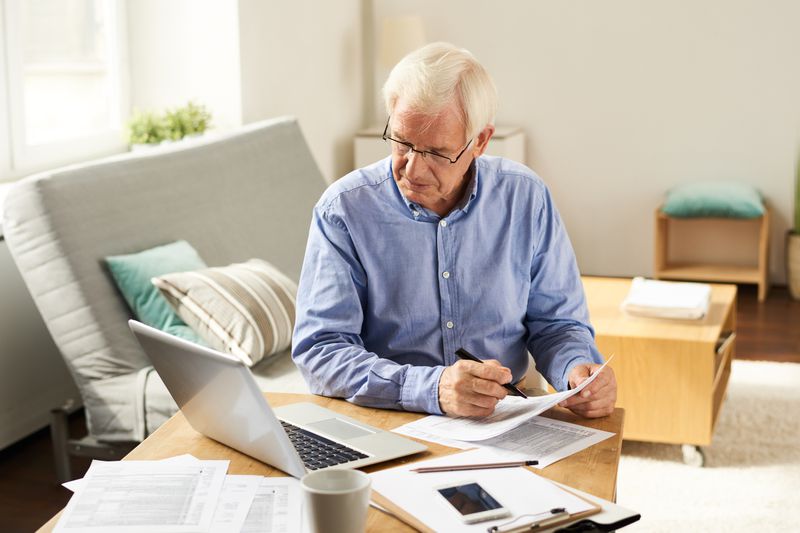 A man filling in application form while sitting at table with laptop in living room.