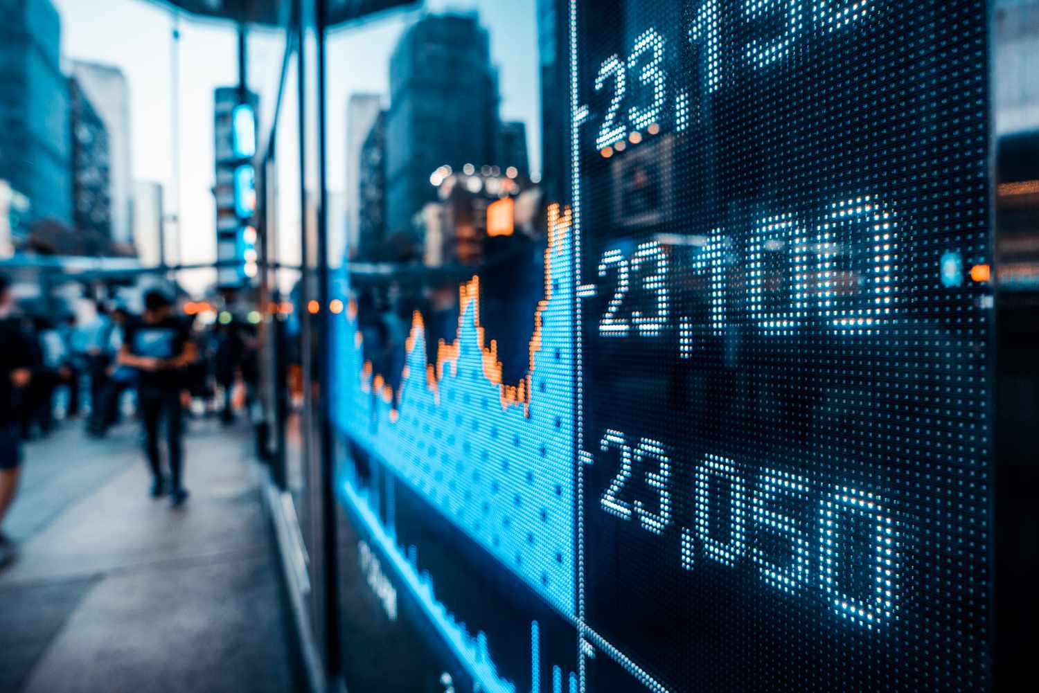 A close-up of a screen displaying a stock market chart as people pass by on the sidewalk