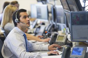 A trader watches price action on a exchange board as they execute orders for clients at a brokerage firm's trading desk.
